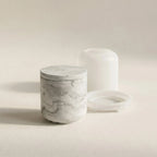 Minimalist grey marble cylindrical jar cast in eco-resin next to its translucent silicone mould set on a cream studio background.
