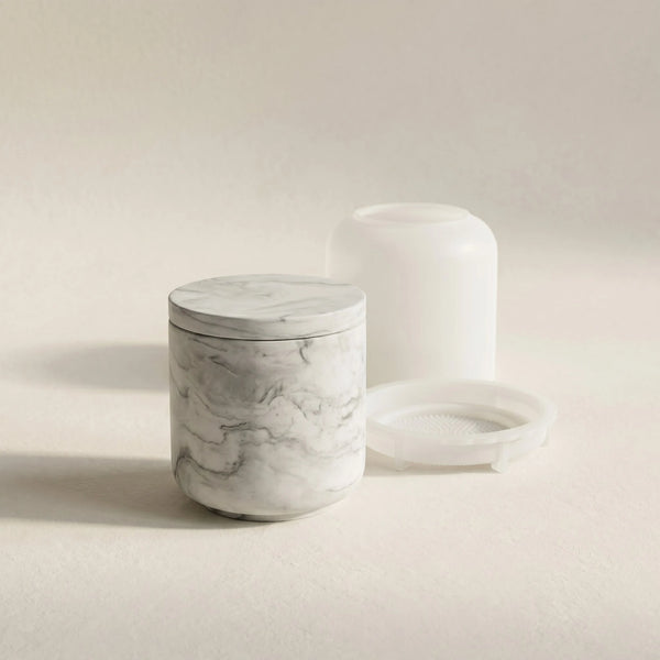 Minimalist grey marble cylindrical jar cast in eco-resin next to its translucent silicone mould set on a cream studio background.